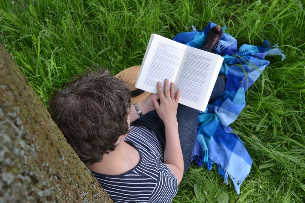 Young woman sits up against a tree reading a book
